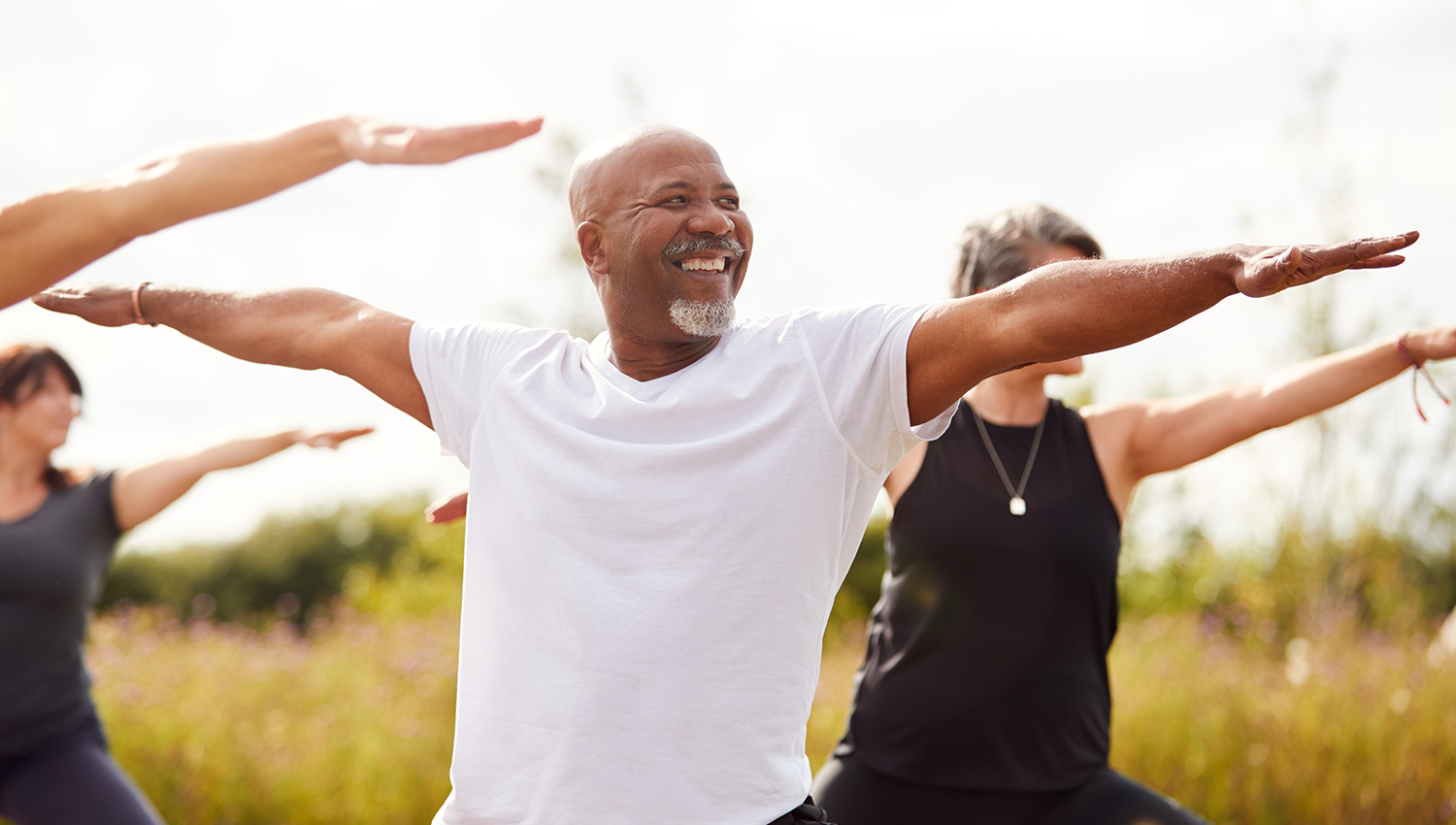 A smiling senior man participating in an outdoor group yoga session as part of a worksite wellness program.